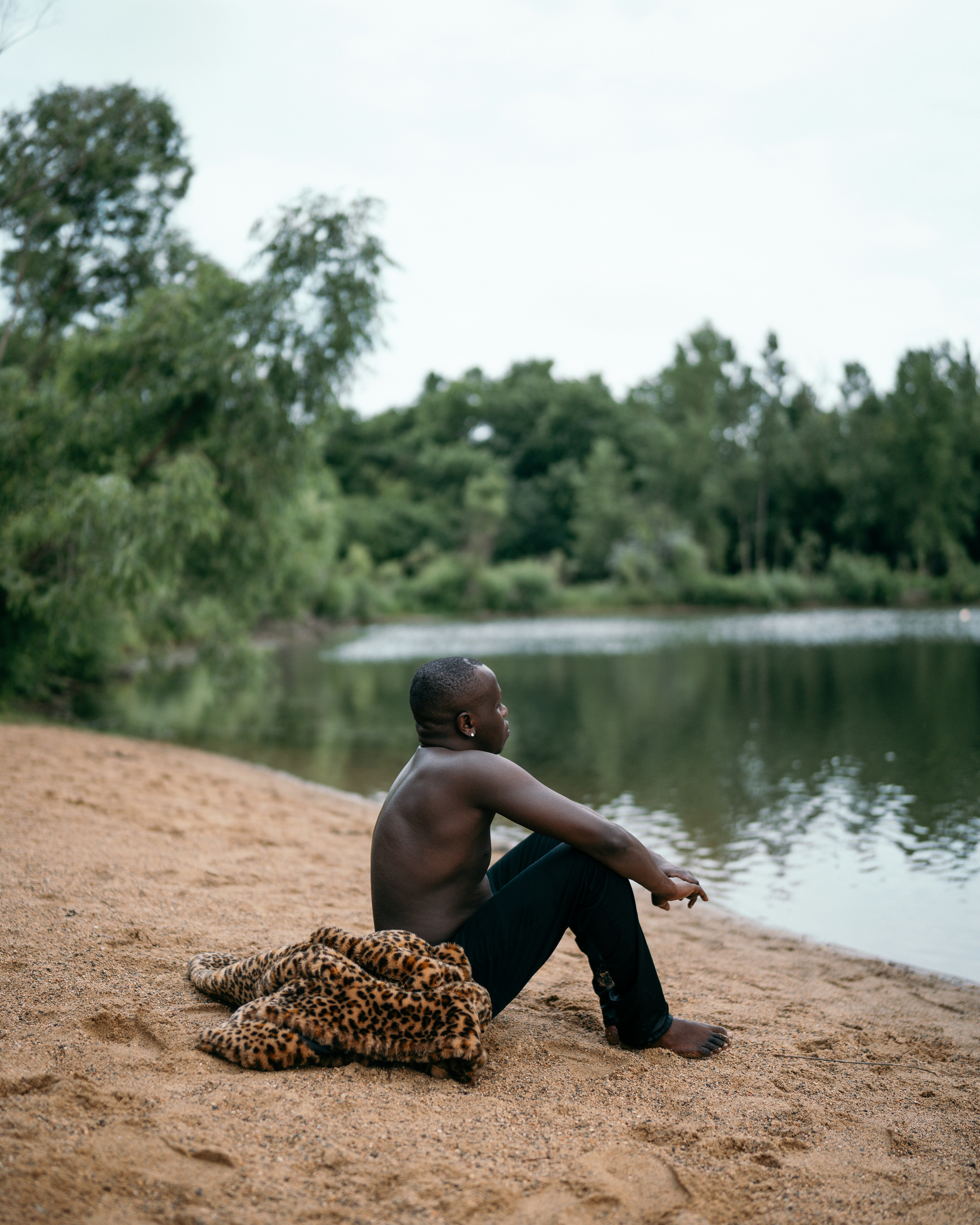 boy in black shorts sitting on brown sand near lake during daytime